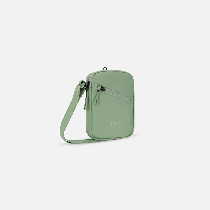 A Sherpani Rogue Olivine Mini Crossbody, 3/4 view showing lockable pocket & strap on white backdrop.  #color_olivine-green