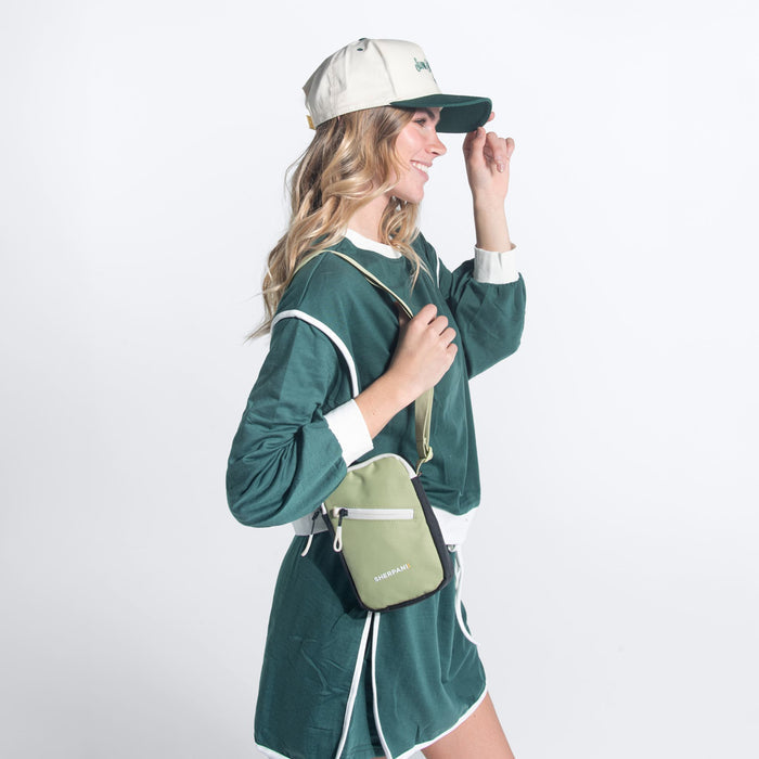 Woman wearing a Sherpani Rogue Palm Green Mini Crossbody on her shoulder against white background. #color_palm-green