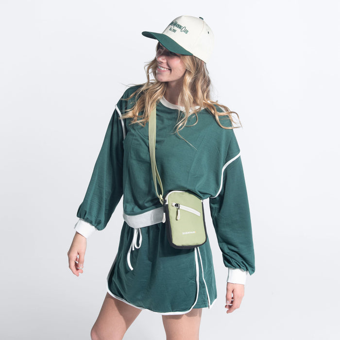 Woman wearing a Sherpani Rogue Palm Green Mini Crossbody against white background.  #color_palm-green