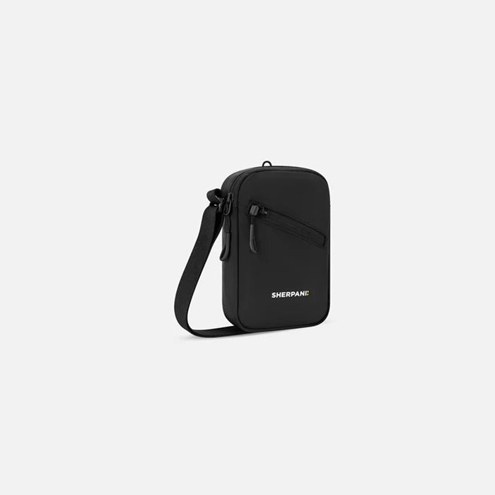 A Sherpani Rogue Raven Black Mini Crossbody, 3/4 view showing lockable pocket & strap on white backdrop.  #color_raven-black