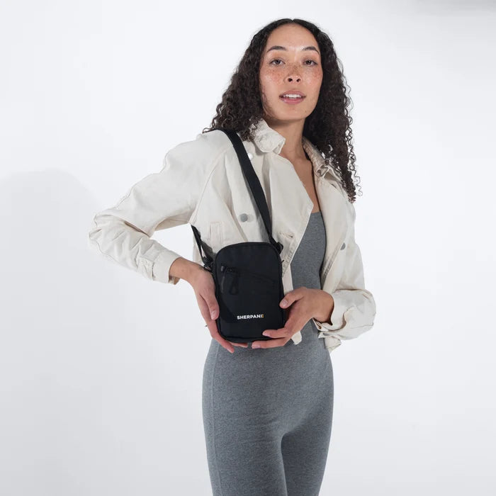 Woman wearing a Sherpani Rogue Raven Black Mini Crossbody on her shoulder against white background.  #color_raven-black