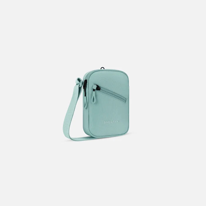 A Sherpani Rogue Surf Blue Mini Crossbody, 3/4 view showing lockable pocket & strap on white backdrop.  #color_surf-blue