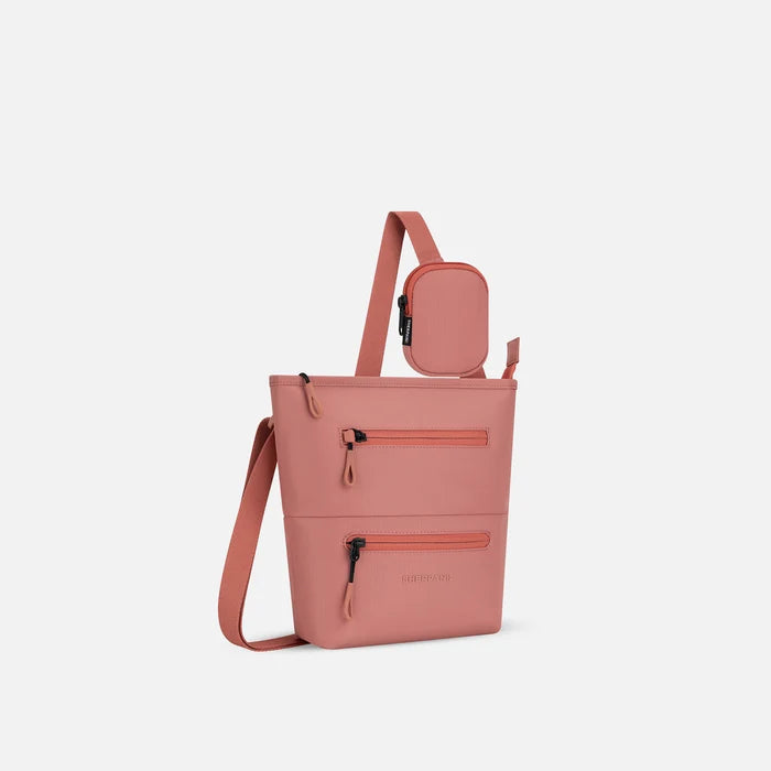 A Sherpani Desert Pink Crossbody Bag, 3/4 view showing front lockable zipper pockets and the pouch attached to the strap. #color_desert-pink