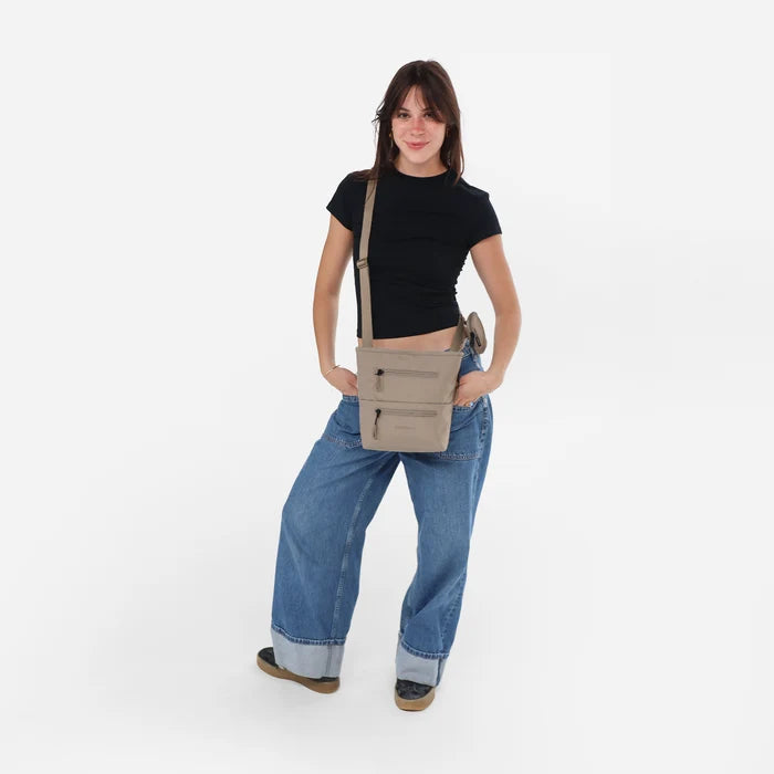 A woman wearing Sherpani Sadie Dune Crossbody Bag against a white background. #color_dune-tan