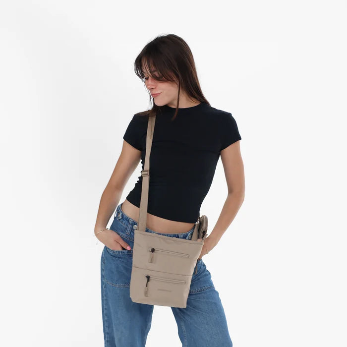 A woman wearing Sherpani Sadie Dune Crossbody Bag against a white background.  #color_dune-tan