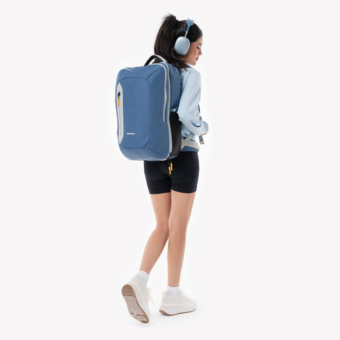 Woman wearing a Sherpani Santiago Seastone Travel Backpack on her back against white backdrop. #color_seastone