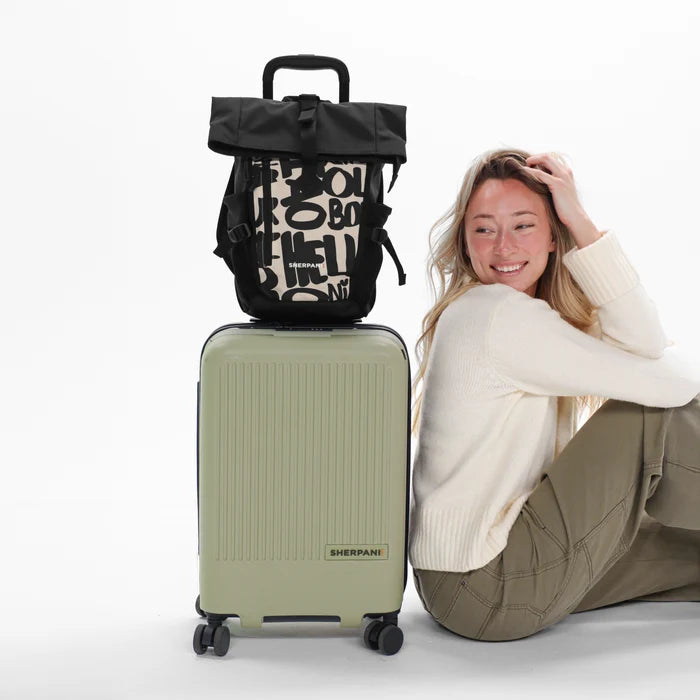 A woman sitting next to a Sherpani Meridian Luggage with a Sherpani Sedona Raven Black Backpack on top against white background. #color_ciao-print