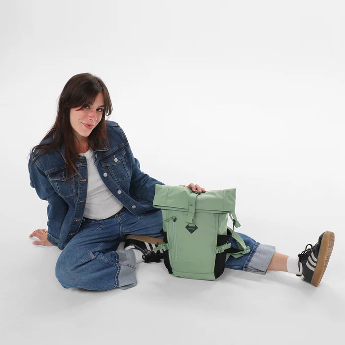 Woman sitting with a Sherpani Sedona Olivine Backpack against white background. #color_olivine-green