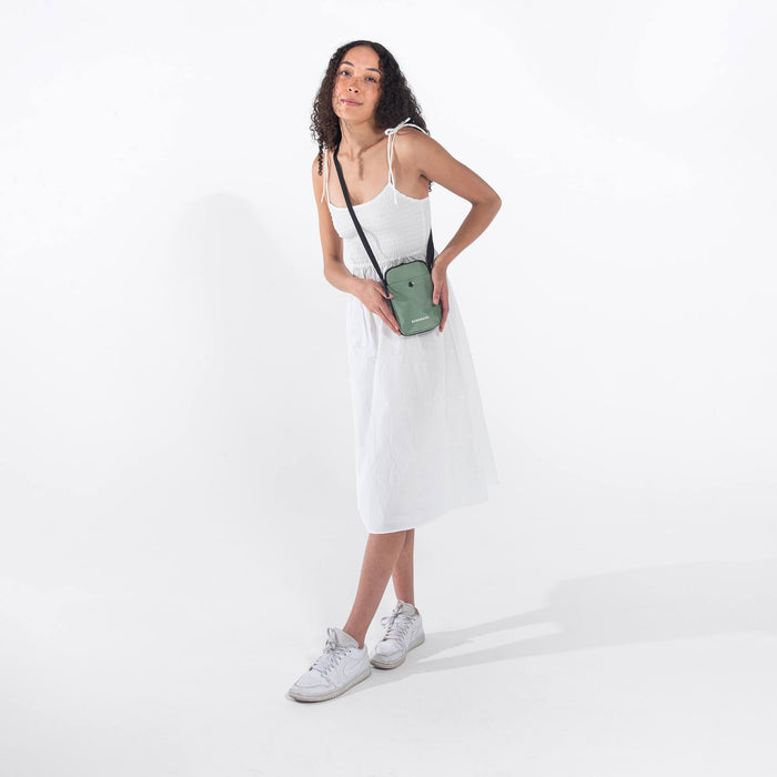 Woman wearing a Sherpani Simplicity Aloe Mist Green Crossbody Wallet against white backdrop. #color_aloe-mist-green