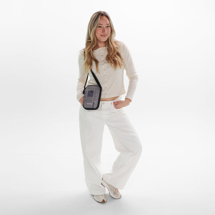 Woman wearing a Sherpani Simplicity Passport Anti-Theft Crossbody Wallet on her shoulder against white backdrop.  #color_passport-print