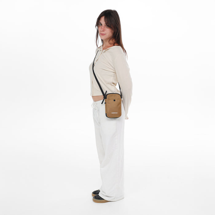 Woman wearing a Sherpani Simplicity  Sand Anti-Theft Crossbody Wallet on her shoulder against white backdrop.  #color_sand-tan