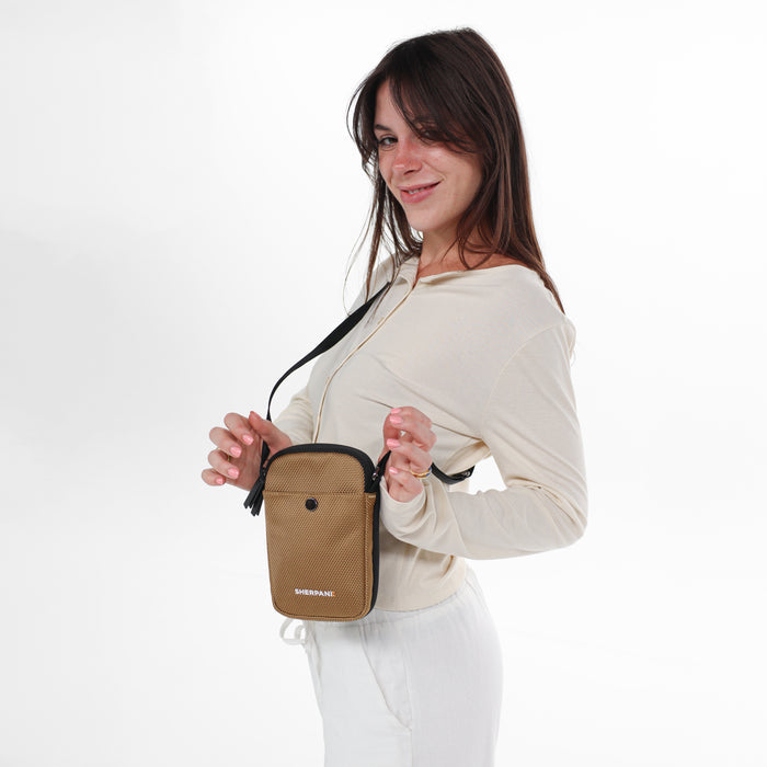 Woman wearing a Sherpani Simplicity Sand Anti-Theft Crossbody Wallet on her shoulder against white backdrop.  #color_sand-tan