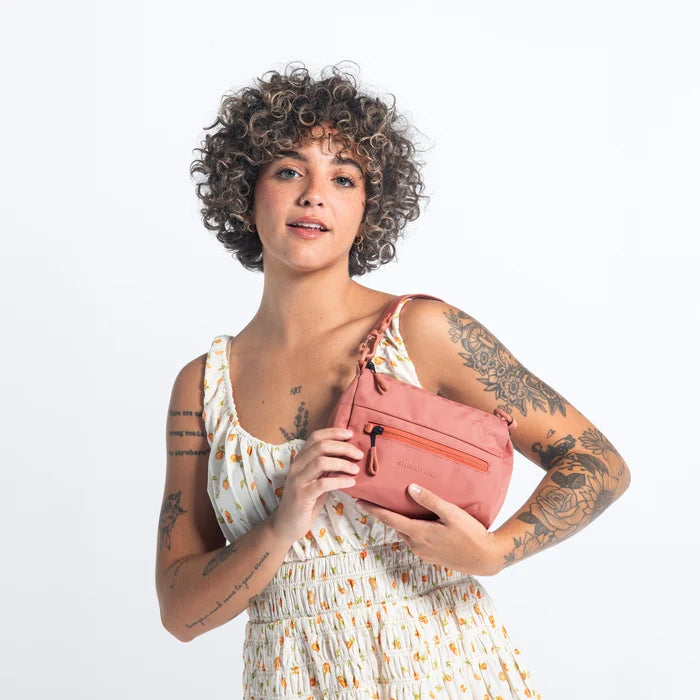 Woman wearing a Sherpani Skye Desert Pink Shoulder Bag by short strap against white backdrop. #color_desert-pink