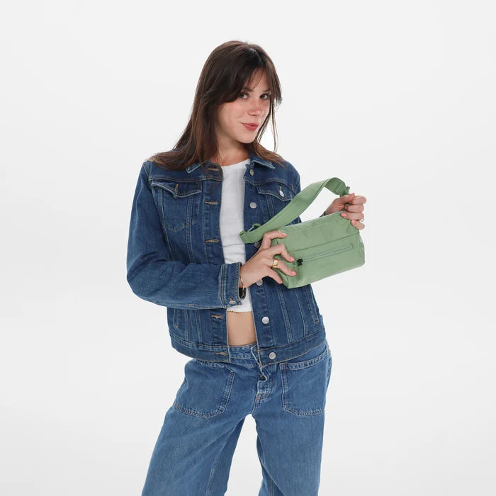 Woman holding a Sherpani Skye Olivine  Shoulder Bag by short strap against white backdrop.#color_olivine-green