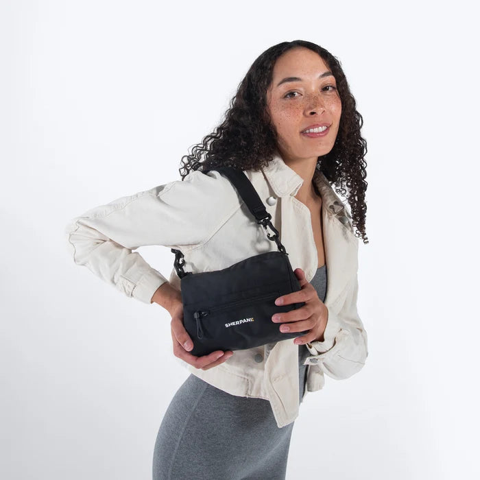 Woman wearing a Sherpani Skye Raven Black Shoulder Bag by short strap against white backdrop. #color_raven-black
