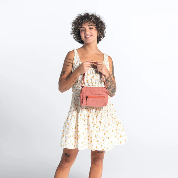 Woman holding a Sherpani Skye Desert Pink Shoulder Bag by short strap against white backdrop. #color_desert-pink