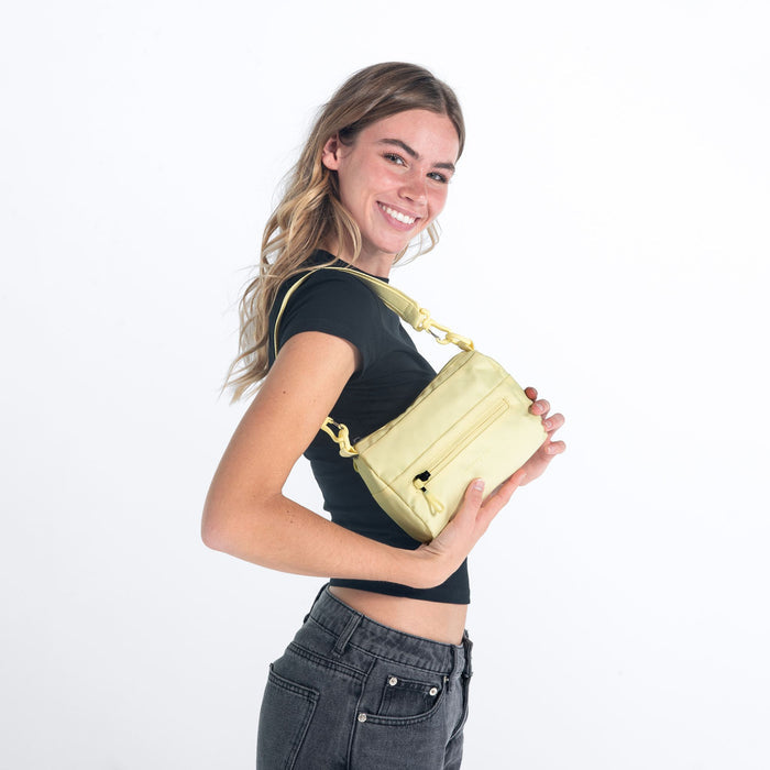 Woman wearing a Sherpani Skye Sol Yellow Shoulder Bag by short strap against white backdrop.  #color_sol-yellow