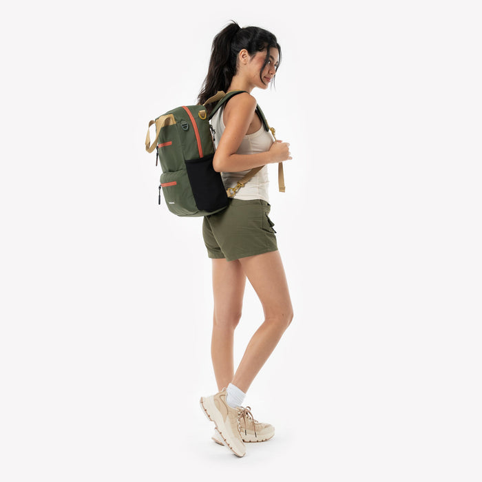Woman wears a Sherpani Sojourn Antelope Multi-Wear Pack on her back against white backdrop. #color_antelope