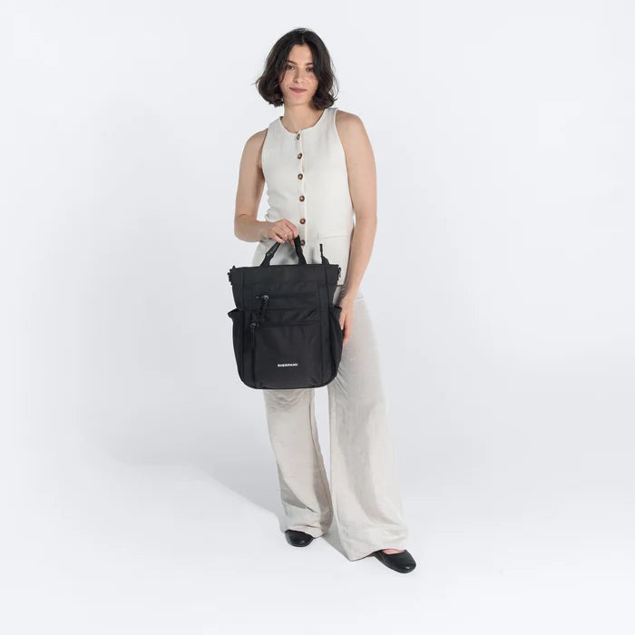 Woman holding Sherpani Soleil Carbon Black Anti-theft Multi-Wear Travel Bag by handheld straps on white backdrop. #color_carbon-black