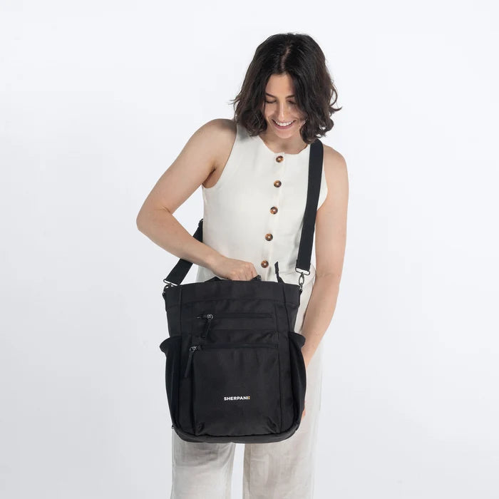 Woman holding Sherpani Soleil Carbon Black Anti-theft Multi-Wear Travel Bag by crossbody straps on white backdrop. #color_carbon-black