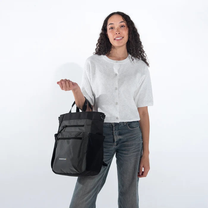 Woman holding Sherpani Soleil Granite Anti-theft Multi-Wear Travel Bag by handheld straps on white backdrop. #color_granite-grey