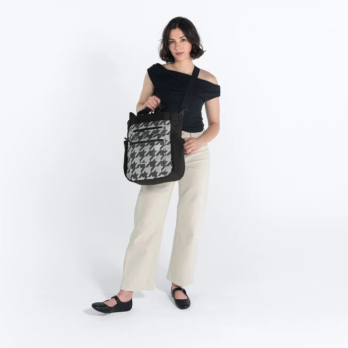 Woman holding Sherpani Soleil Houndstooth Anti-theft Multi-Wear Travel Bag by crossbody straps on white backdrop. #color_houndstooth-print