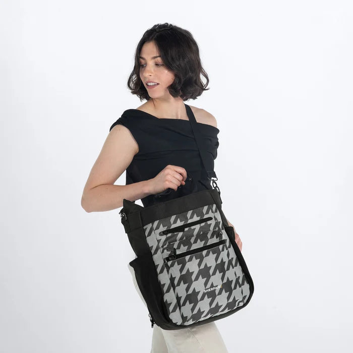 Woman holding Sherpani Soleil Houndstooth Anti-theft Multi-Wear Travel Bag by crossbody straps on white backdrop. #color_houndstooth-print