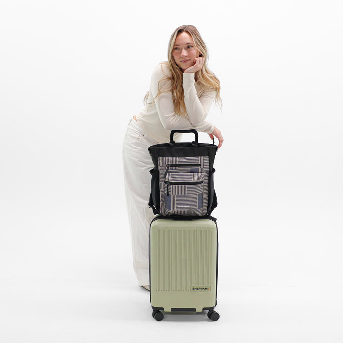 Woman holds Sherpani Soleil Passport Anti-theft Multi-Wear Travel Bag on Sherpani Meridian Matcha Carry-On on a white backdrop.  #color_passport-print