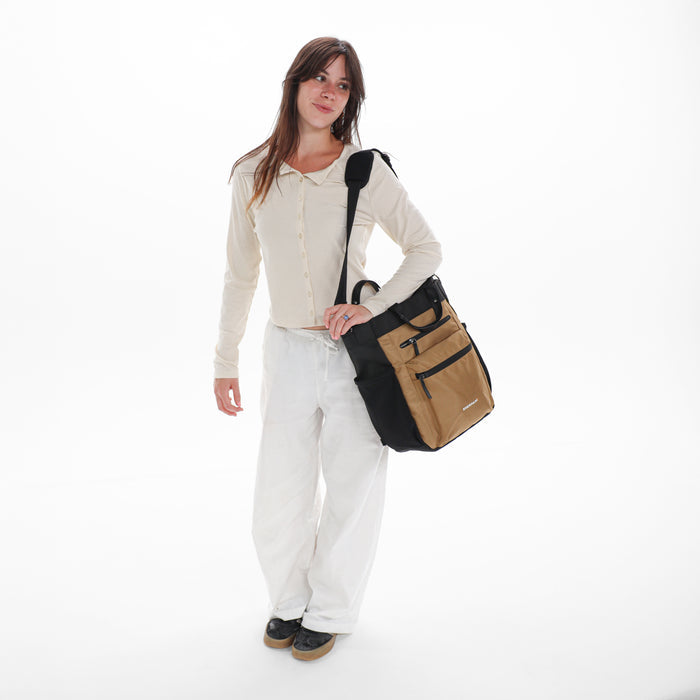 Woman holding Sherpani Soleil Sand Anti-theft Multi-Wear Travel Bag by crossbody straps on white backdrop. #color_sand-tan