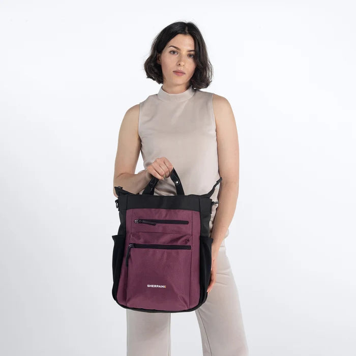 Woman holding Sherpani Soleil Smoky Orchid Anti-theft Multi-Wear Travel Bag by handheld straps on white backdrop. #color_smoky-orchid-pink