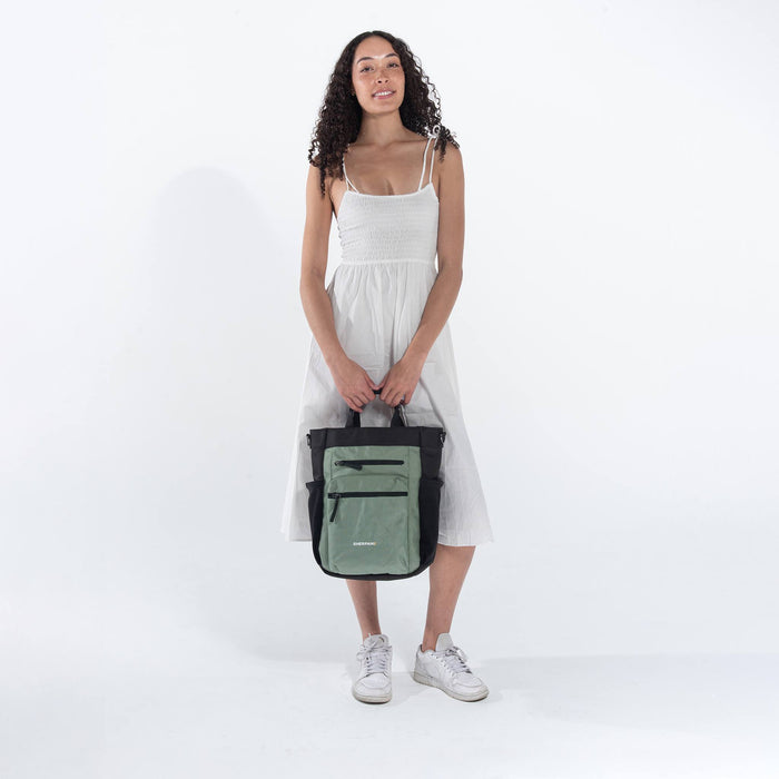 Woman holding Sherpani Soleil Aloe Mist Green Anti-theft Multi-Wear Travel Bag by handheld straps on white backdrop. #color_aloe-mist-green