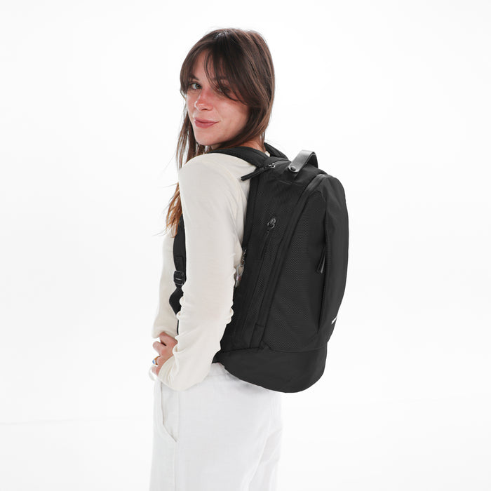 A woman wearing a Sherpani Solstice Carbon Black Anti-Theft Travel Backpack on her back against a white background.   #color_carbon-black