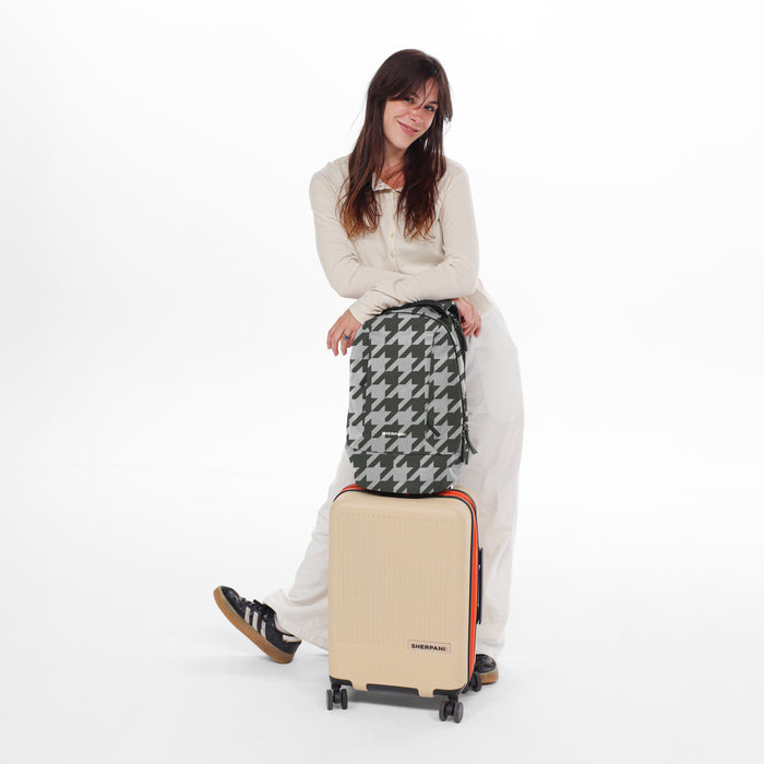 A woman holding a Sherpani Solstice Houndstooth Anti-Theft Travel Backpack on top of a Sherpani Meridian Luggage. #color_houndstooth-print