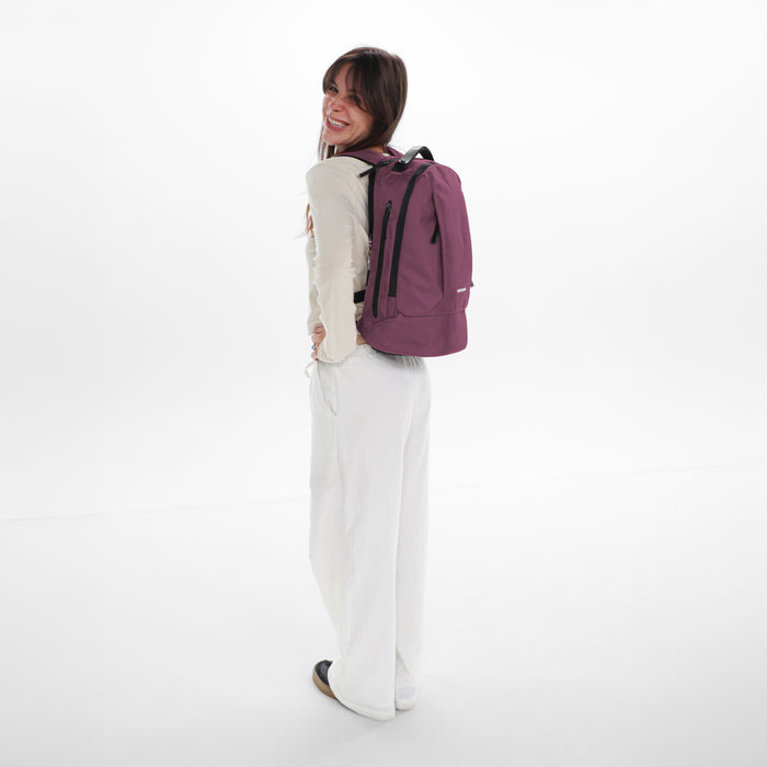 A woman wearing a Sherpani Solstice Smoky Orchid Anti-Theft Travel Backpack on her back against a white background.   #color_smoky-orchid-pink