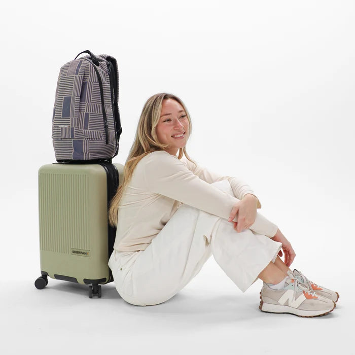 A woman sitting next to a Sherpani Solstice Passport Anti-Theft Travel Backpack on top of a Sherpani Meridian Luggage.  #color_passport-print