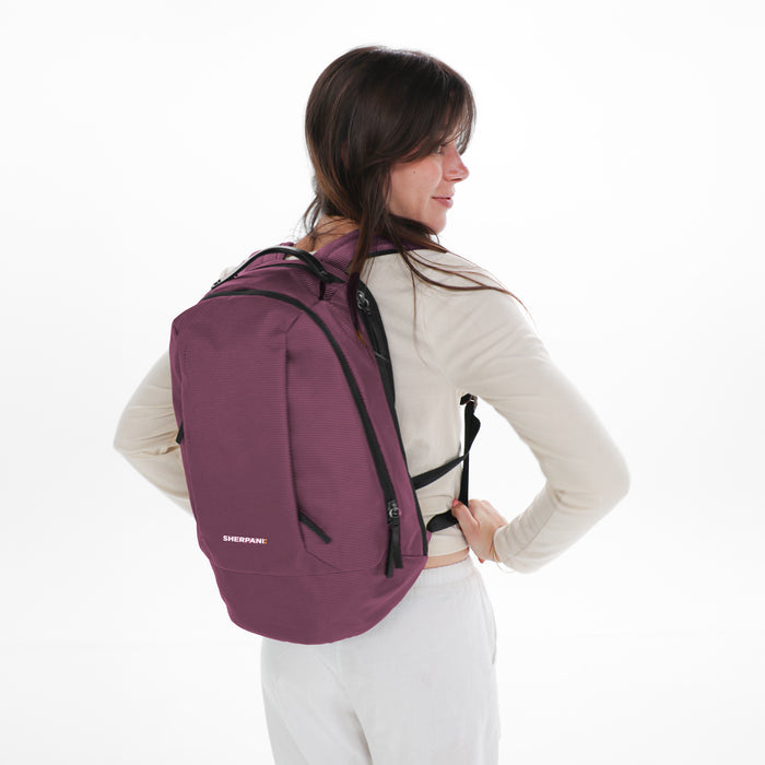 A woman wearing a Sherpani Solstice Smoky Orchid Anti-Theft Travel Backpack on her back against a white background.   #color_smoky-orchid-pink