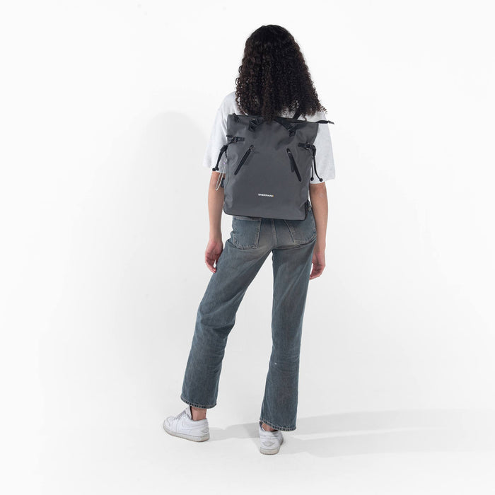 Woman wearing a Sherpani Tempest Granite Grey Convertible Tote on her back against white background.  #color_granite-grey