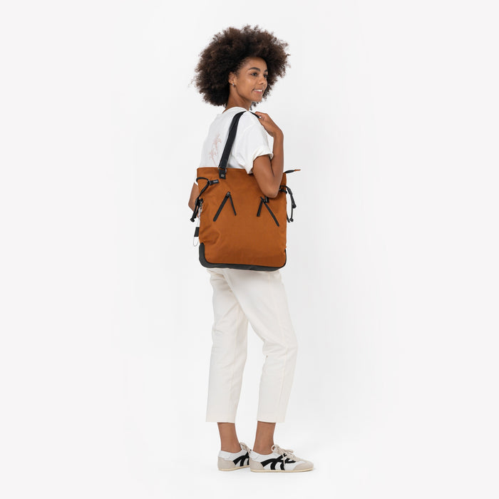 Woman wearing a Sherpani Tempest Morocco Convertible Tote on her shoulder against white background. #color_morocco