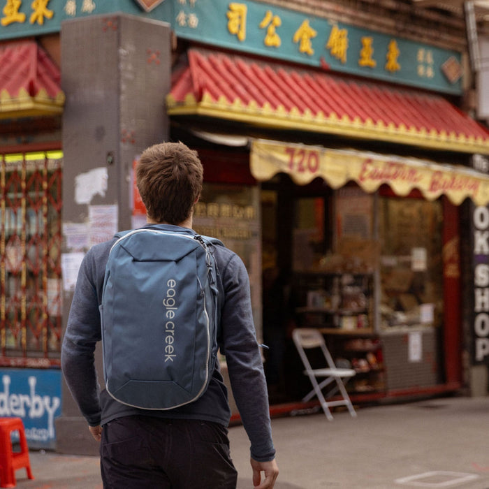 A person wearing a blue travel backpack outside of a shop.