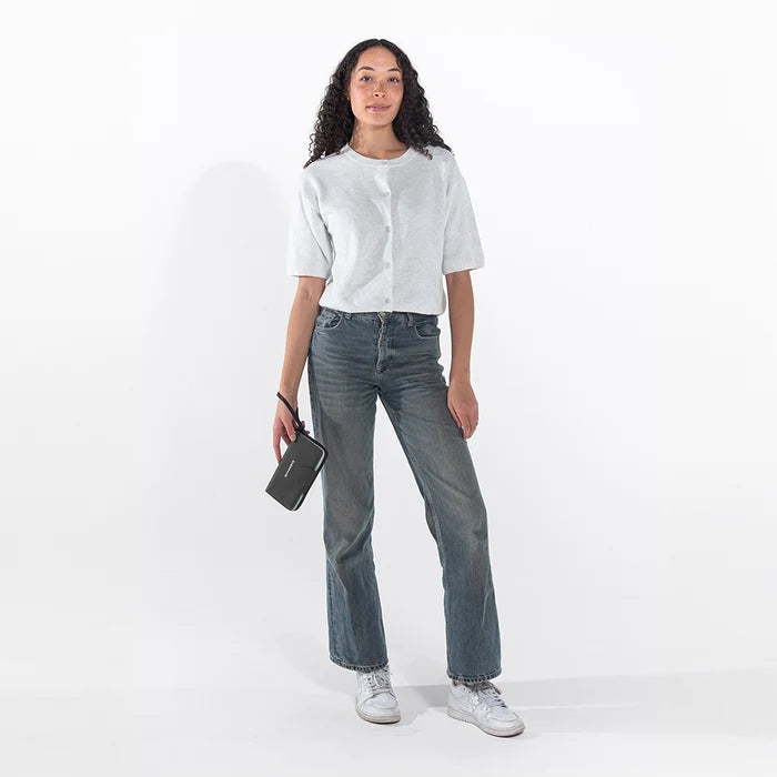 Woman holding a Sherpani Tulum Granite Anti-Theft Wallet by wrist strap against white background. #color_carbon-black