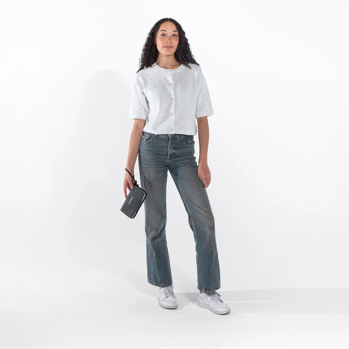 Woman holding a Sherpani Tulum Granite Anti-Theft Wallet by wrist strap against white background. #color_granite-grey