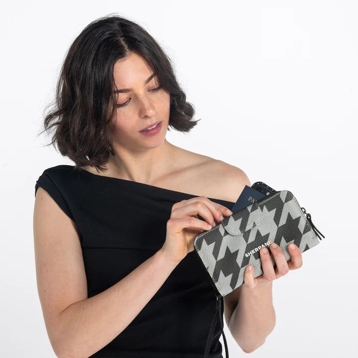 Woman placing a passport into a Sherpani Tulum houndstooth Anti-Theft Wallet against white background. #color_houndstooth-print