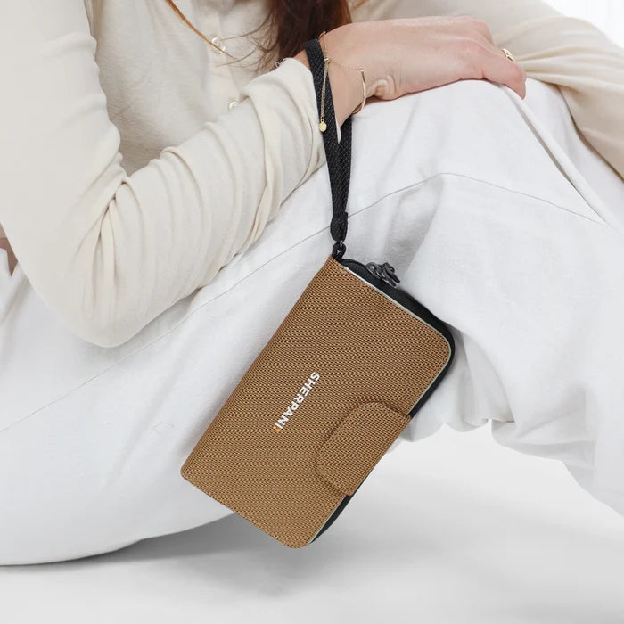Woman holding a Sherpani Tulum Sand Anti-Theft Wallet by wrist strap against white background.  #color_sand-tan