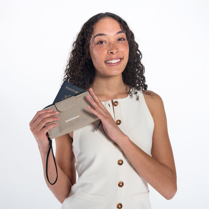 Woman holds a Sherpani Tulum Straw Beige Anti-theft RFID Wallet with passport inside against white background.  #color_straw-beige