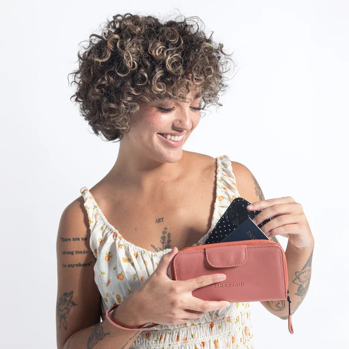 Woman placing a phone into a Sherpani Tulum Desert Pink RFID Wallet against white background.   #color_desert-pink
