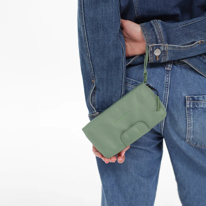 Woman holding a Sherpani Tulum Olivine RFID Wallet by wrist strap against white background.   #color_olivine-green