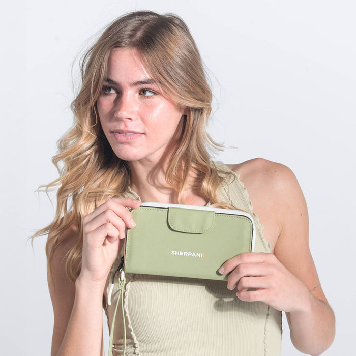 Woman holds a Sherpani Tulum Palm Green RFID Wallet against white background.  #color_palm-green