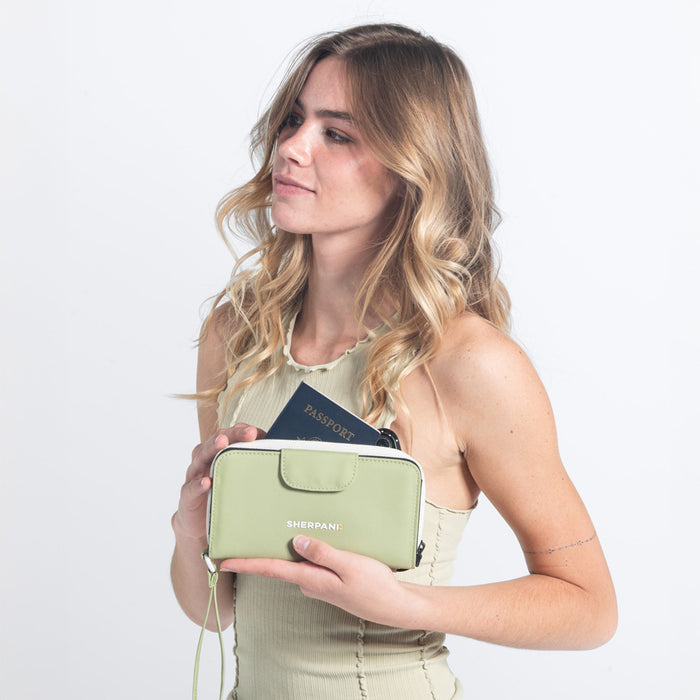 Woman holds a Sherpani Tulum Palm Green RFID Wallet with passport inside against white background.  #color_palm-green