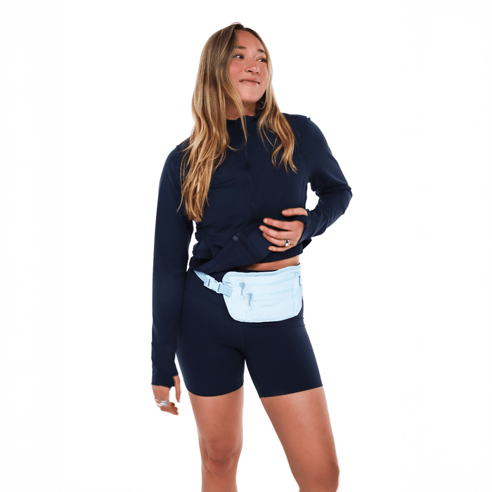 Woman with a Sherpani Soft Touch Concealed Waist Wallet Cool Blue around her waist on white background.