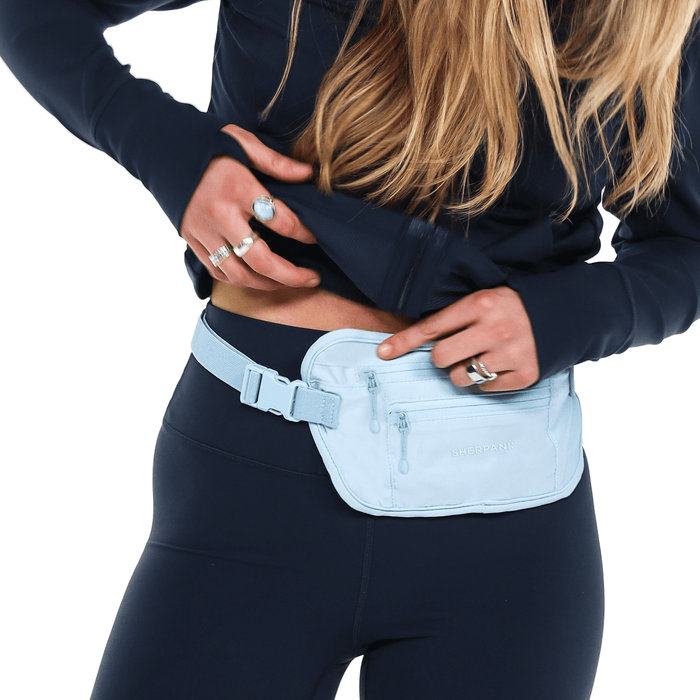 Woman with a Sherpani Soft Touch Concealed Waist Wallet Cool Blue around her waist on white background.